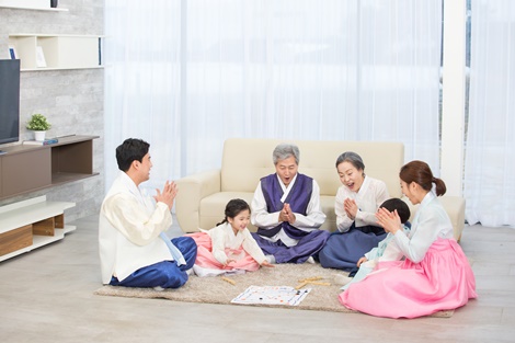 한복을 입고 있는 여섯명의 가족들이 거실에 모여 윷놀이를 하고 있는 사진
