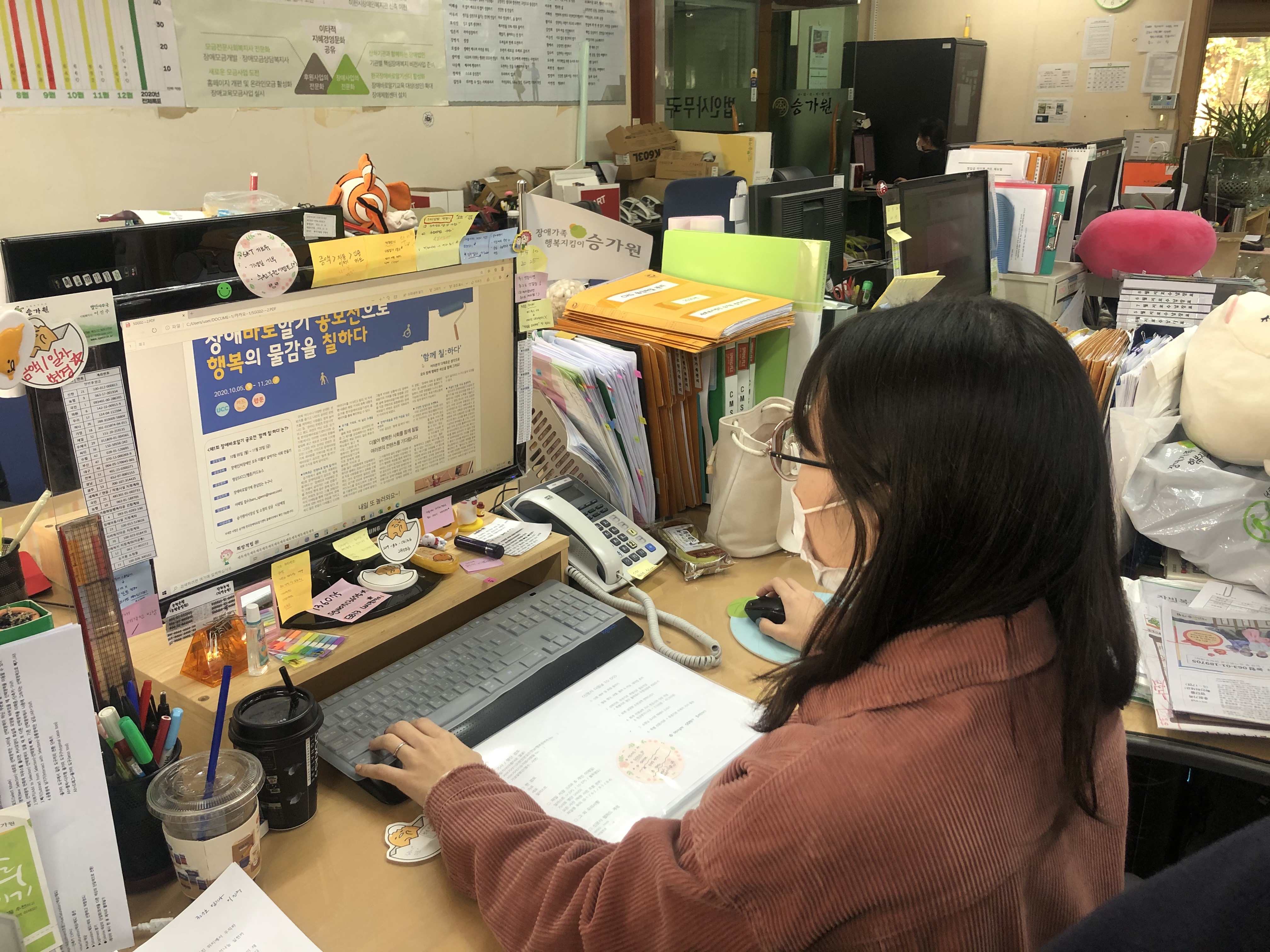 신문제작 작업을 위해 '장애바로알기 공모전으로 행복의 물감을 칠하다'라고 적혀있는 신문판을 보고 있는 여자 근무가족