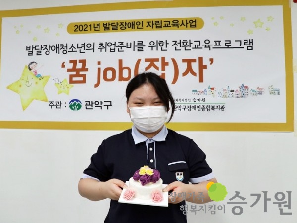 발달장애청소년의 취업준비를위한 전환교육프로그램 꿈job(잡)자 라는 문구가 써져있는 현수막 앞에서 케이크를 들고 사진을 찍은 참여자의 모습