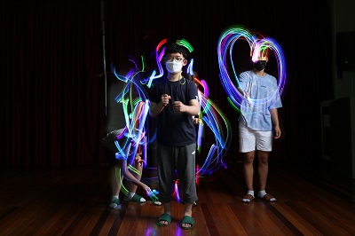불이 꺼진 깜깜한 공간에서 라이트스틱을 가지고 놀고 있는 3명의 참여자 여러 색깔의 빛으로 몸의 실루엣을 만들고 있다.