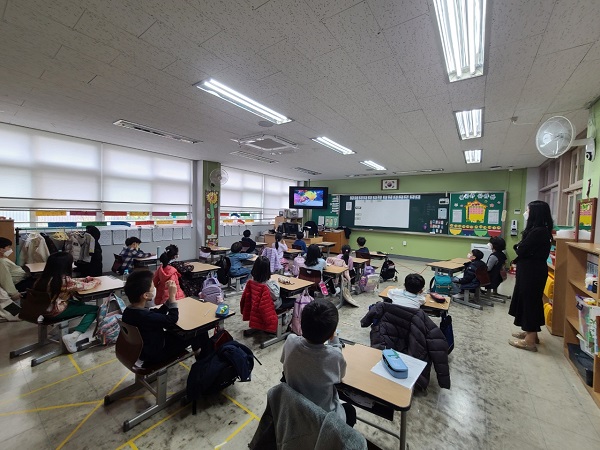 초등학교 교실에 아이들이 앉아있고 칠판과 화면을 바라보며 이론교육에 집중하고 있다.