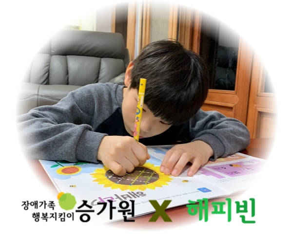 아동이 펜을 쥐고 공부하는 사진. 해피빈 X장애가족행복지킴이 승가원 CI