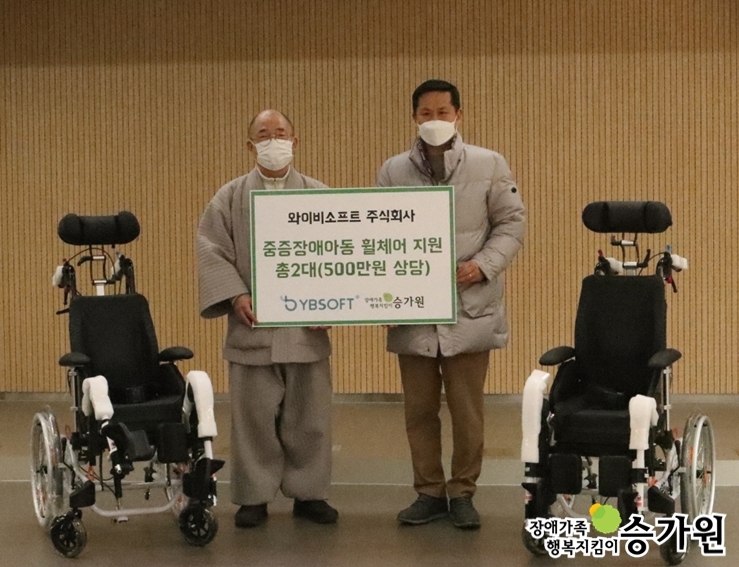국장스님과 주식회사와이비소프트 대표이사가 휠체어 전달식을 하고 있는 모습. 양옆에 휠체어가 한 대씩 놓여있음./ 장애가족행복지킴이 승가원CI