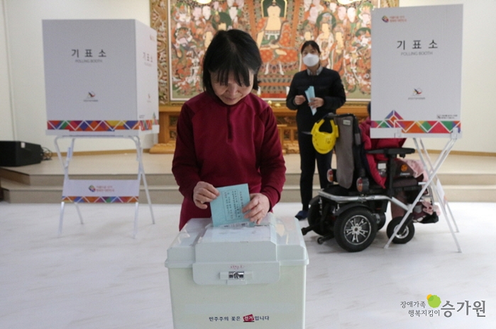 투표함에 투표용지를 넣는 여성 장애가족 / 오른쪽 하단에 장애가족행복지킴이 승가원 CI