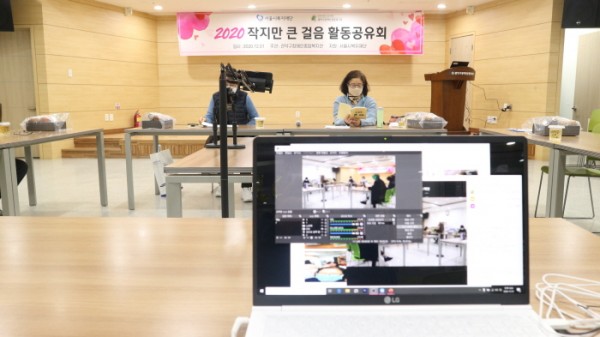 상단에 '2020 작지만 큰 걸음 활동공유회'라는 현수막이 위치해있다. 그 아래 책상에 앉은 2명의 주민 대표가 노트북으로 온라인 공유회를 진행하는 화면이 보이고 있다.