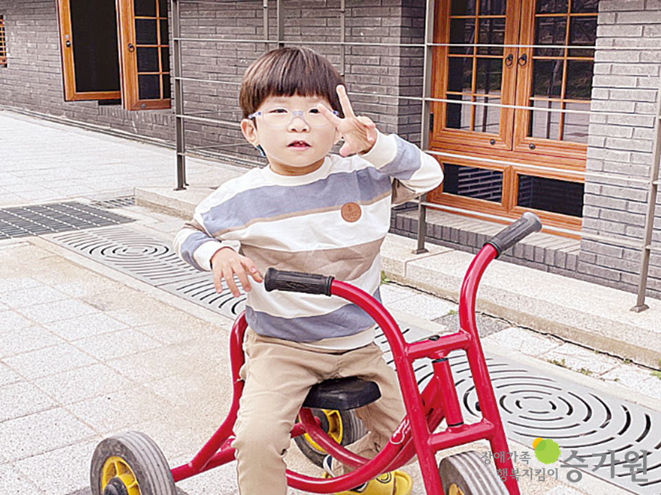 CI삽입 장애가족 행복지킴이 승가원,행복마을 앞마당에서 밝은 표정으로 빨간색 세발자전거를 타고 있는 안태양 어린이의 모습