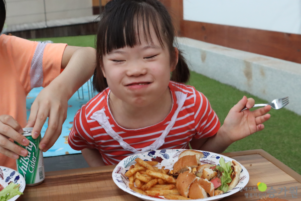 CI 삽입 장애가족 행복지킴이 승가원, 포크를 들고 양볼 가득 햄버거를 먹고 있는 여자 장애아동 