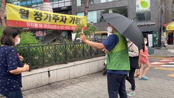 장애가족행복지킴이 승가원 ci삽입/ 비오는 날 우산을 쓰고 있는 근무가족이 길거리 시민들에게 행복나눔캠페인의 참여를 권유하고 있다.