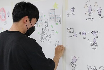 벽에 붙은 종이위에 색연필을 사용해 그림을 그리고 있는 남성 참여자