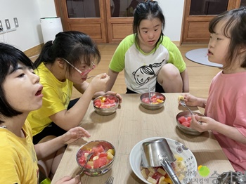 직접만든 과일 화채를 맛있게 먹고 있는 여자 장애아동 4명의 사진/오른쪽 하단에 장애가족행복지킴이 승가원 CI로고 삽입