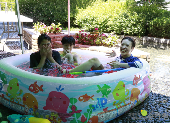 세 명의 남자 장애가족이 작은 고무 풀장에 앉아서 물놀이를 하며 즐거워하고 있다./오른쪽 하단에 장애가족행복지킴이 승가원 CI로고 삽입