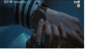 왼손에 손목시계를 차고 오른쪽 검지손가락으로 시계 표면을 가리키고 있는 드라마의 한 장면