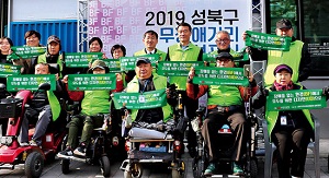 2019 성북구 무장애거리 선포식에 참여한 무장애마을 만들기 참여자들의 모습, 모두 장애물 없는 환경(BF)에서 모두를 위한 디자인(UD)로 라고 적힌 작은 현수막을 들고 있다.