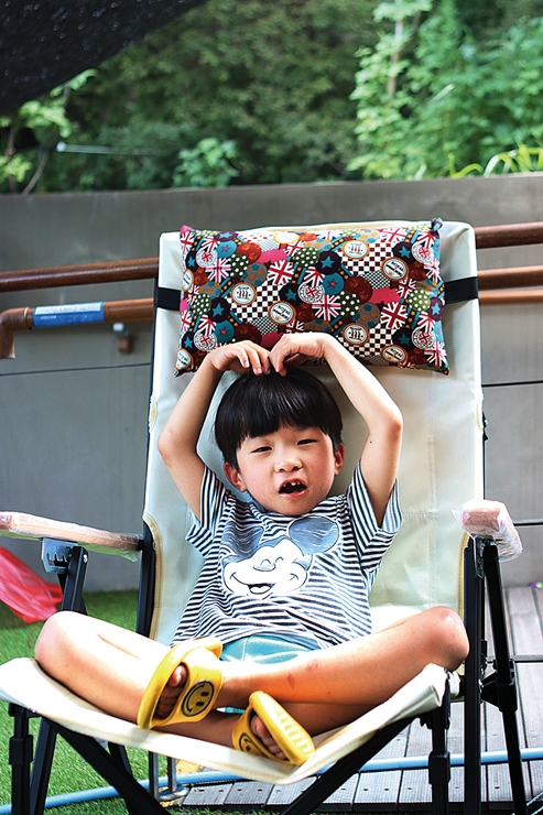 장애아동이 캠핑의자에 앉아 두 손 머리위로 하트를 만들며 웃고 있는 모습