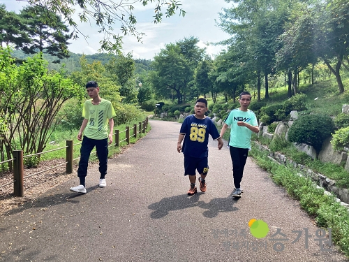 세명의 남자 장애가족이 산책길에서 운동을 하고 있는 모습 푸른 나무가 있는 산책길을 걷고 있다 우측하단 장애가족행복지킴이 승가원 ci 로고 삽