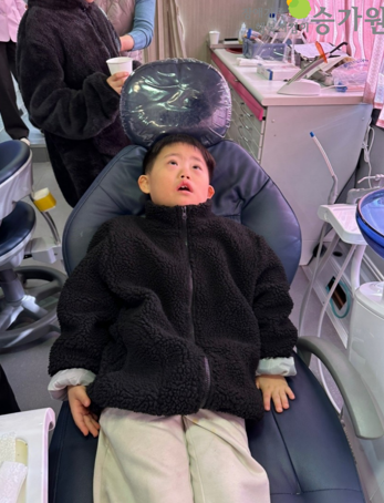 장애아동이 치과 의자 (파란색)에 입을 벌리고 누워있다. 근처에는 치과 장비들이 놓여져 있다. 우측 상단 승가원 ci 삽입